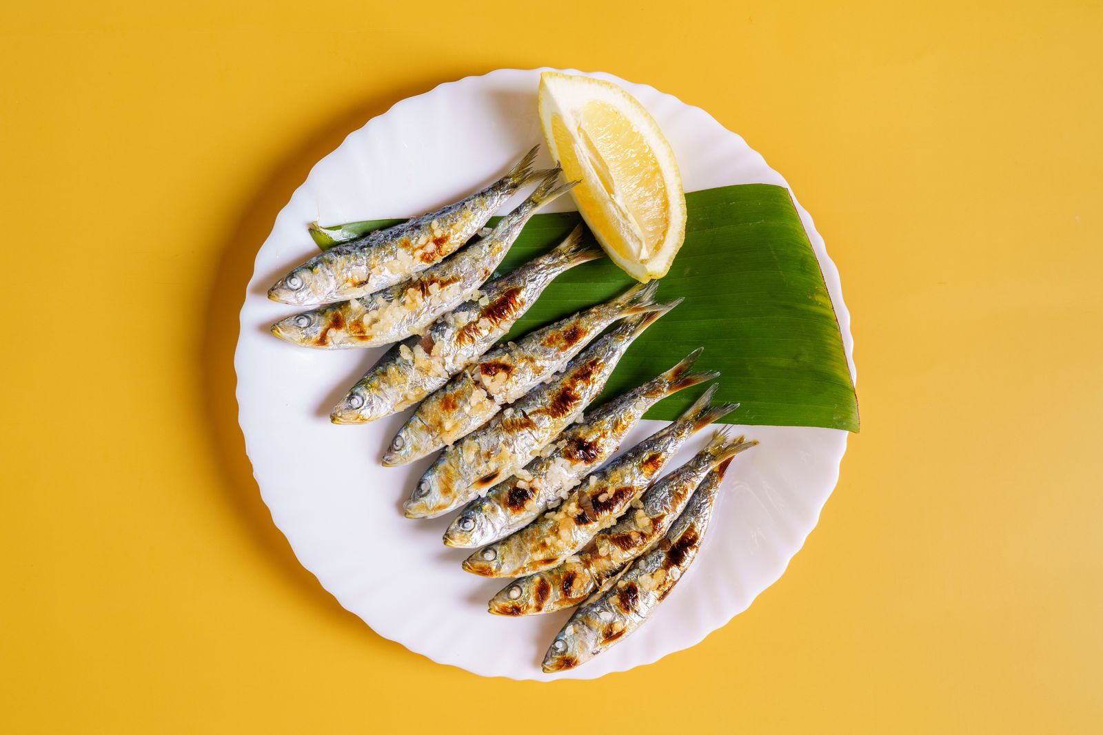 Directly above view of plate of grilled sardines espetos on yellow background